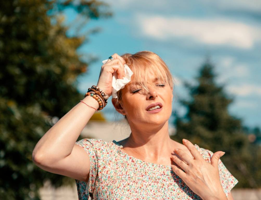 Woman feeling bad pain, heat, woman with heatstroke. Having sunstroke at summer hot weather. Mature Female under sunshine suffering from Headache. Person holds wet tissue on head and cooling with hand palm, heat exhaustion