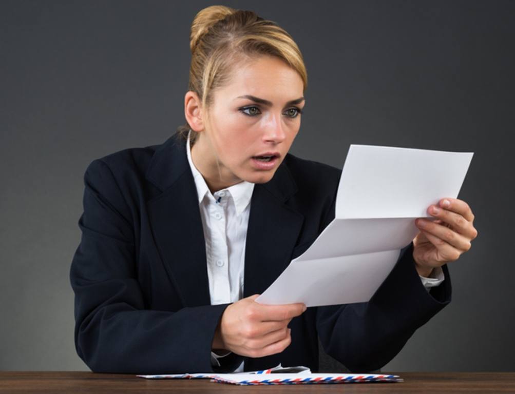 Shocked Young Businesswoman Reading Letter At Desk