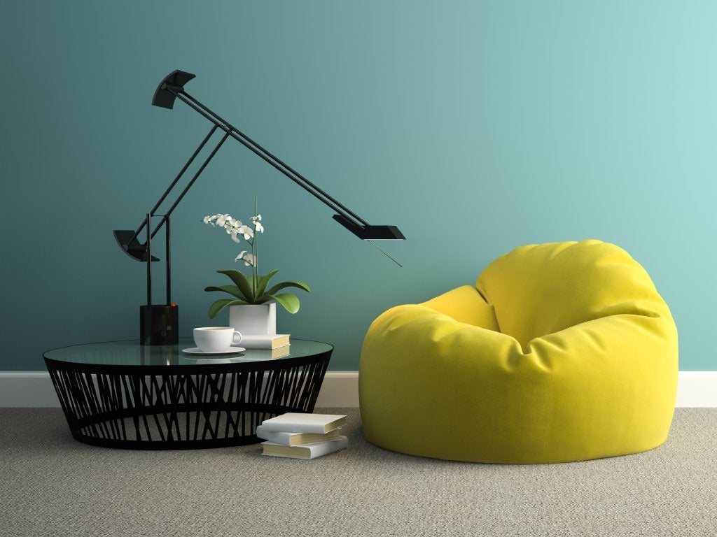 A living room with a teal accent wall, black metal table with a glass top and extending lamp next to a lime beanbag chair.