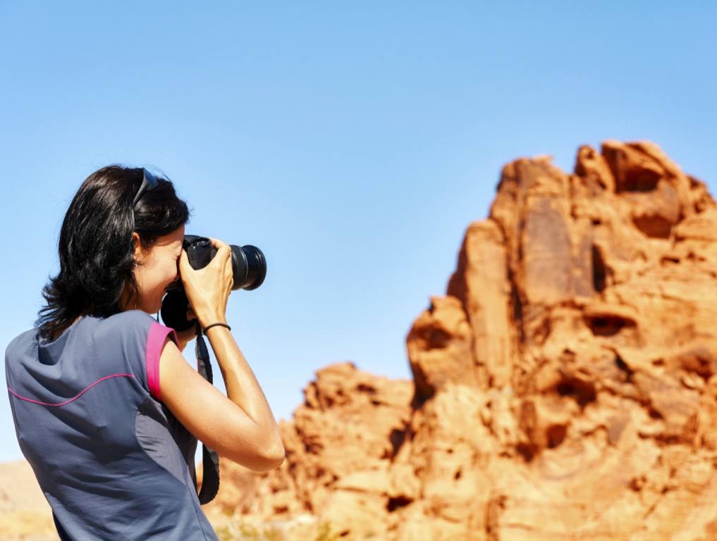 A dark haired woman on the left is standing away from the camera as she takes a picture of a rock formation in the distance. Nevada State Parks concept.