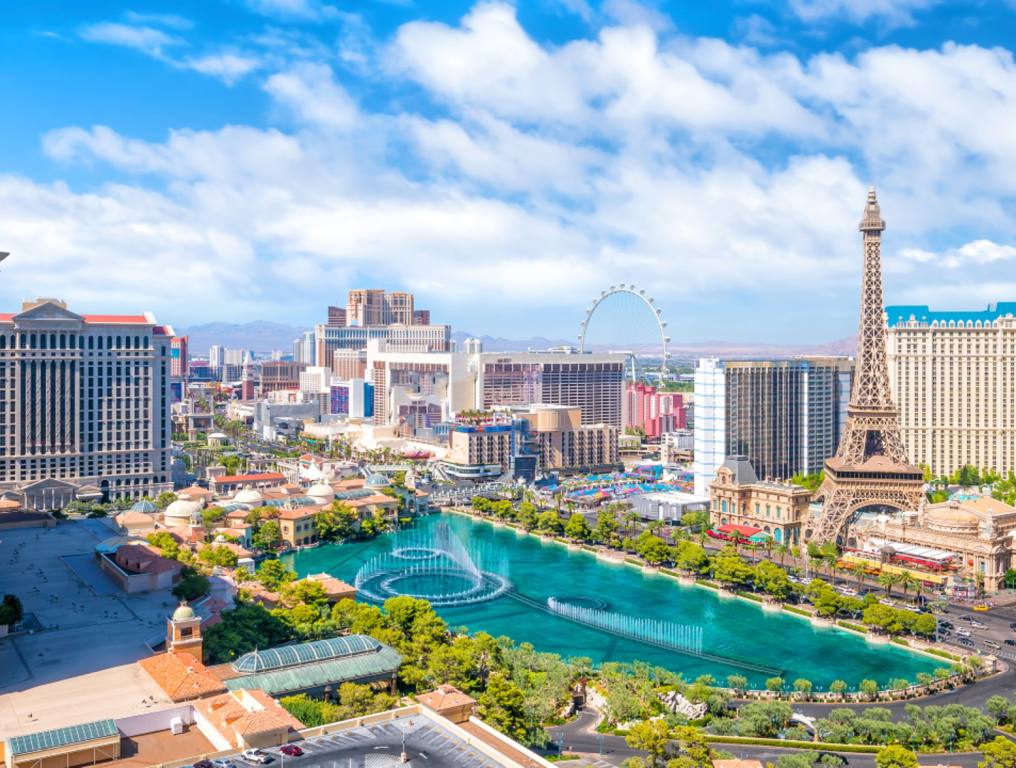 The world famous Las Vegas Strip has been named one of the top 20 U.S. tourist attractions. Wide angle photo from the southern end of Las Vegas Boulevard from a high vantage point. It is a sunny day in Las Vegas with fluffy clouds above. The Bellagio fountains are occupy the center of the photo. Other recognizable attractions include the Eiffel Tower at Paris Las Vegas on the right. The High Roller at the Linq can be seen beyond that. The main tower at Caesars Palace is visible on the left.