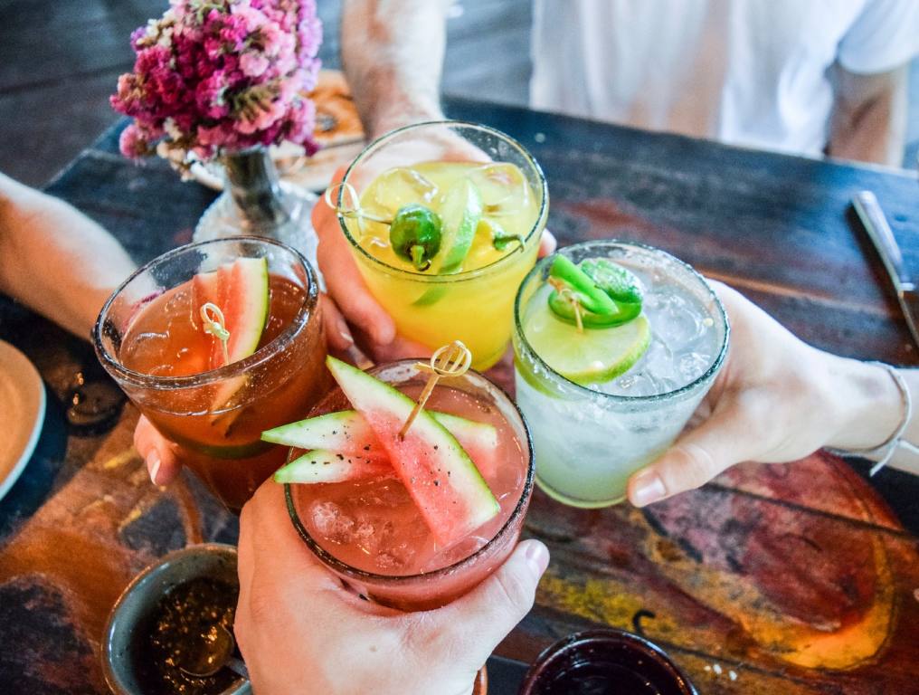 A new Mexican restaurant offering an exciting cocktail menu will soon open in Northwest Las Vegas. Photo of four hands meeting in the middle of a table. Each hand is holding a Mexican margarita cocktail, each with a different type of tropical juice, including pineapple, passionfruit, watermelon, and the classic flavor. These patrons are toasting each other before taking the first sip of their cocktails.