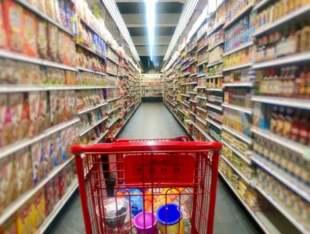 A shopping cart in the middle of an aisle in a grocery store.