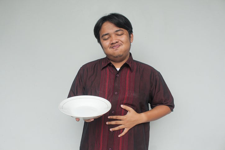 Asian young man holding empty plate and her stomach with happy and full expression.