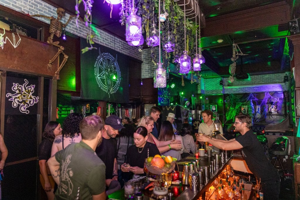 A bar decorated with Halloween decor has many guests sitting around a long bar table.