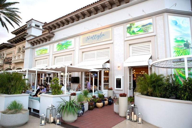 Exterior shot of an Italian shows white architecture, patio seating and green pottery.