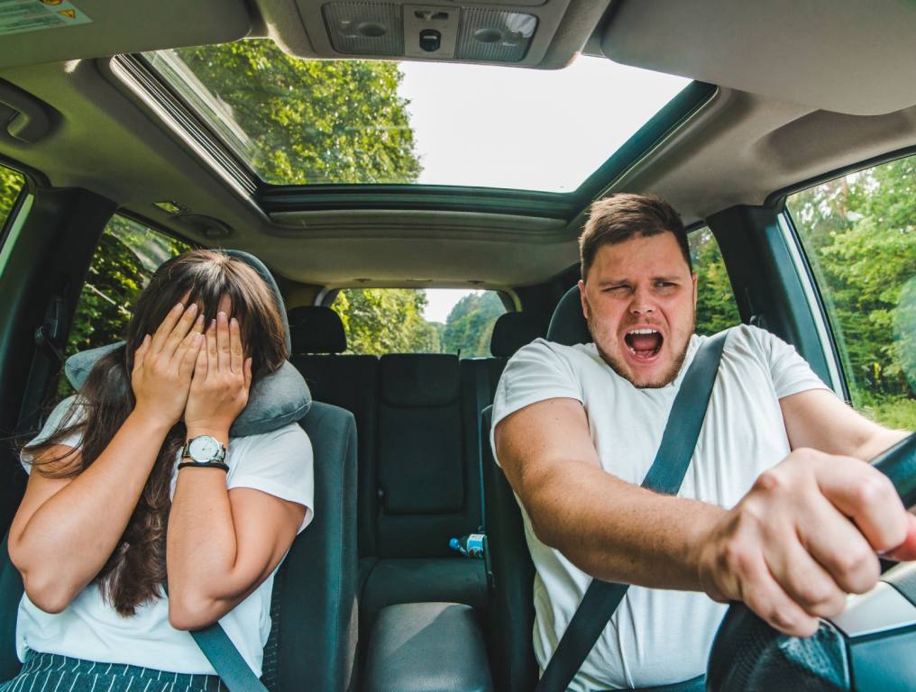 A man in a white t-shirt is driving a car and looking scared while a female passenger in a white t-shirt covers her face in fear. Concept: Las Vegas drivers