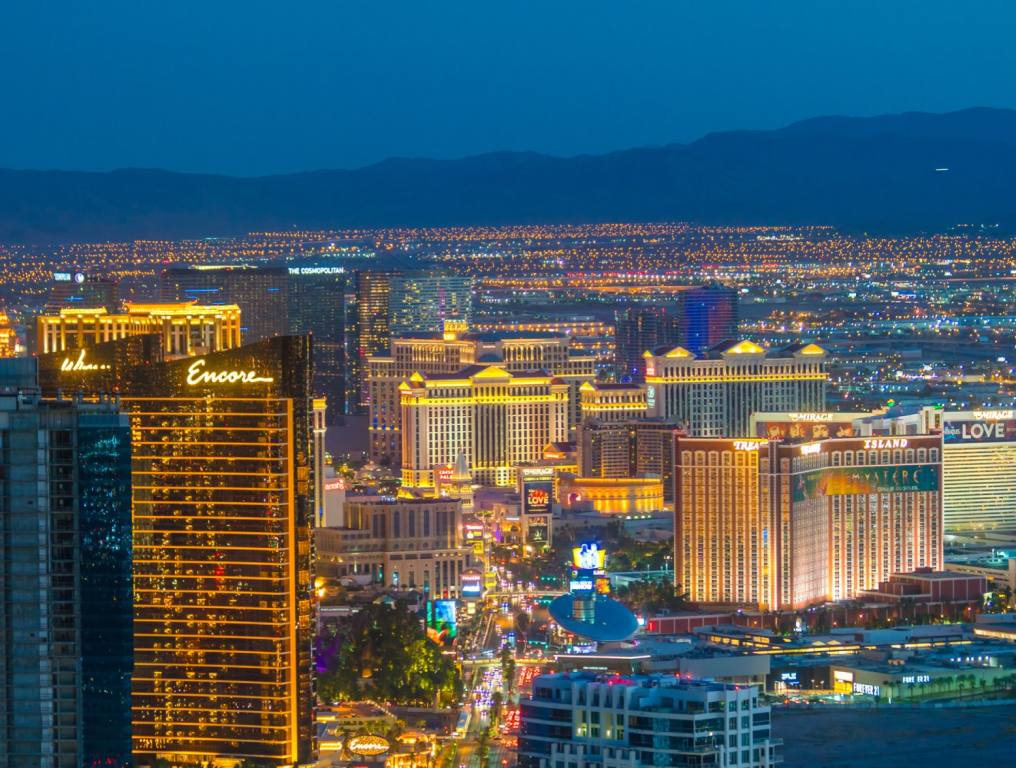 Aerial view of the Las Vegas Strip at sunset shows a light blue sky with mountains in the background and lit up casino hotels. Concept: famous streets