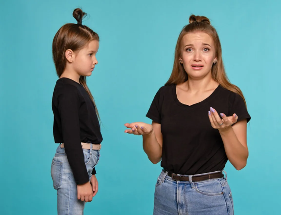 Mom and daughter with a funny hairstyles, dressed in black shirts and blue denim jeans are posing against a blue studio background. Close-up shot