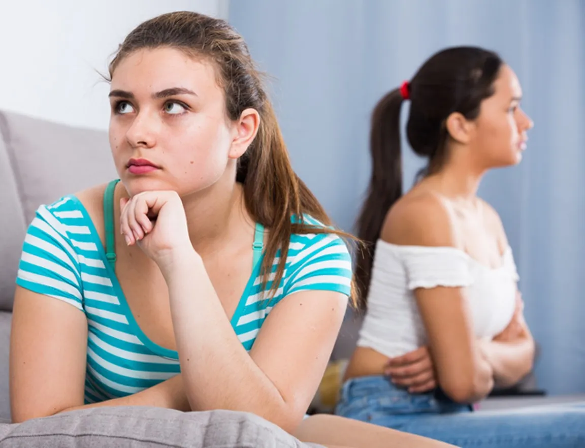 teenage girls sitting apart on couch at home, friend breakup concept.