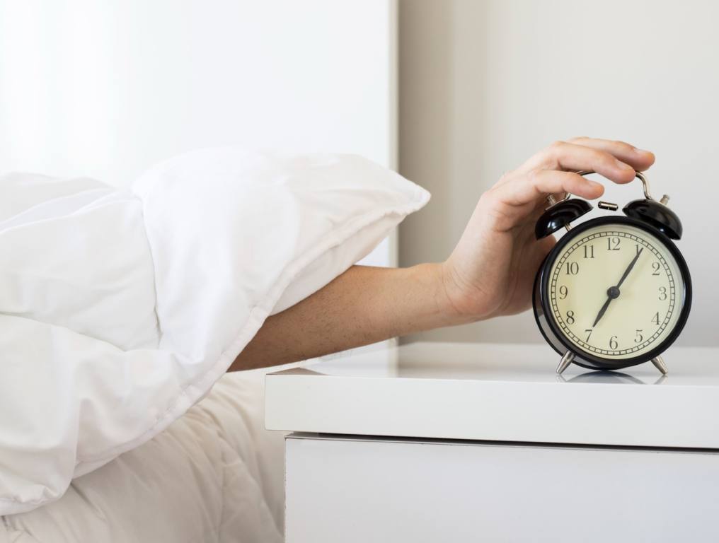 A hand reaching out to hit the snooze on the alarm clock.