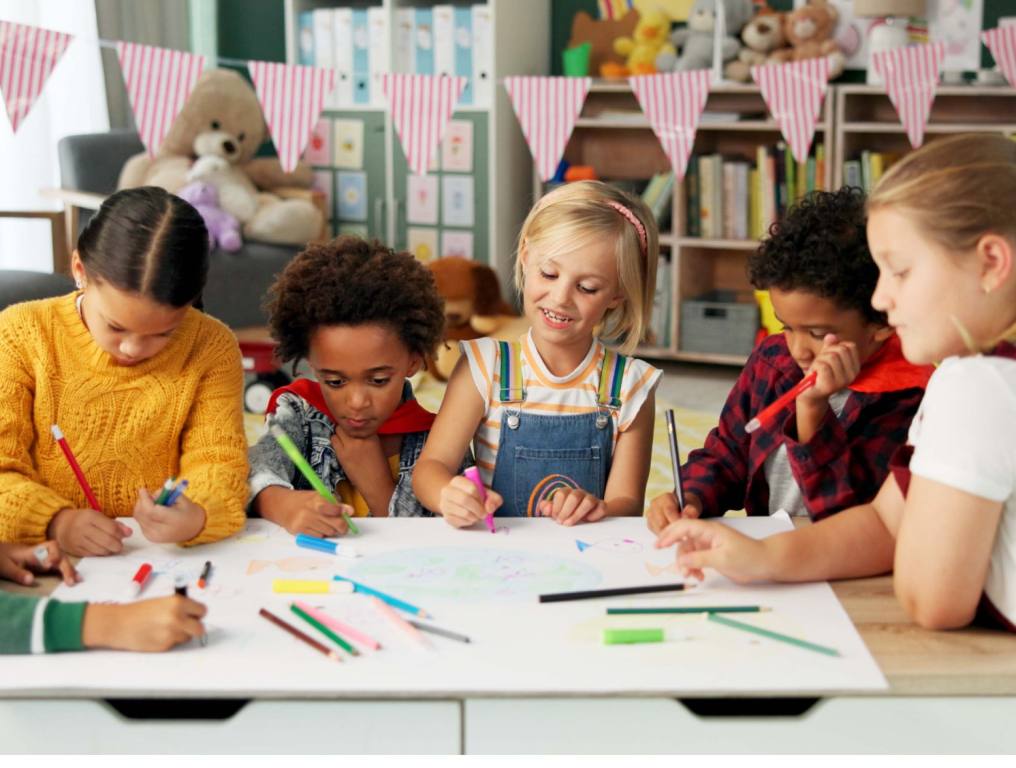 Diverse group of elementary school kids in the classroom are writing in their notebooks and smiling. Concept: school supply drive