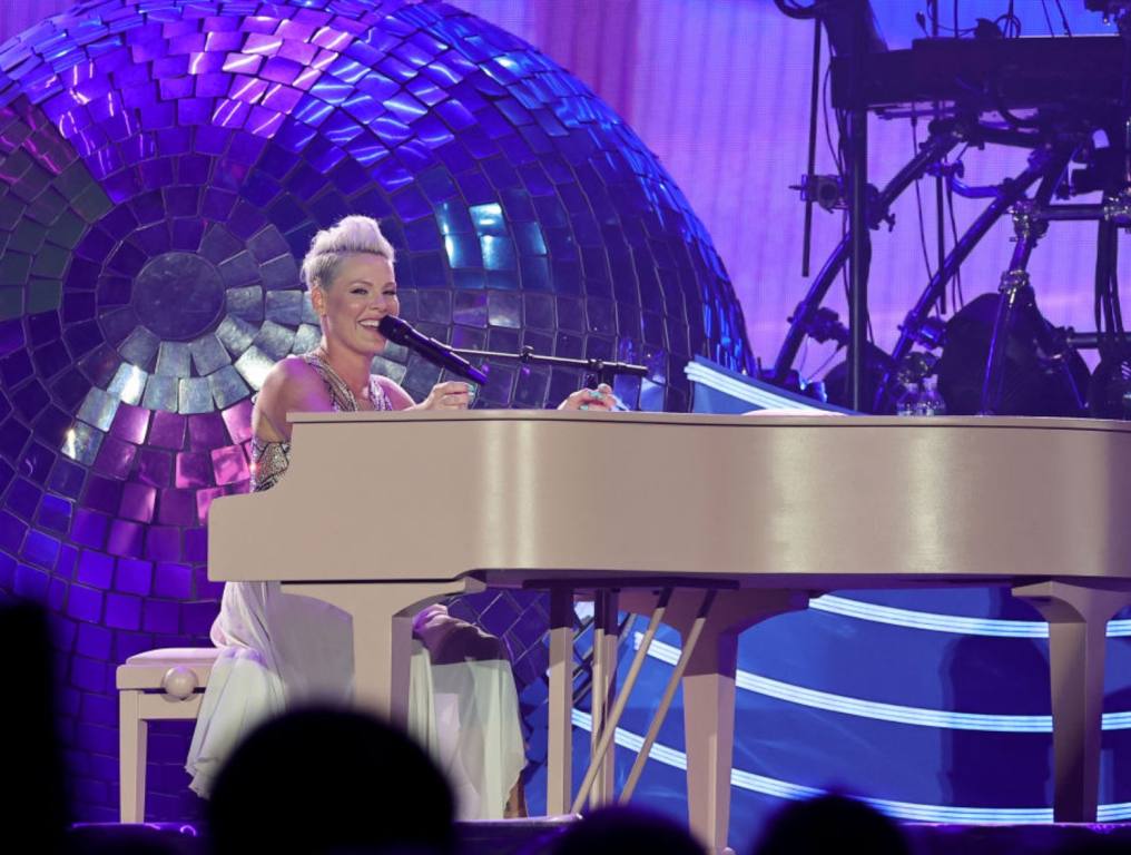 Singer Pink is playing a white piano and singing on stage in concert. Concept: Pink tickets