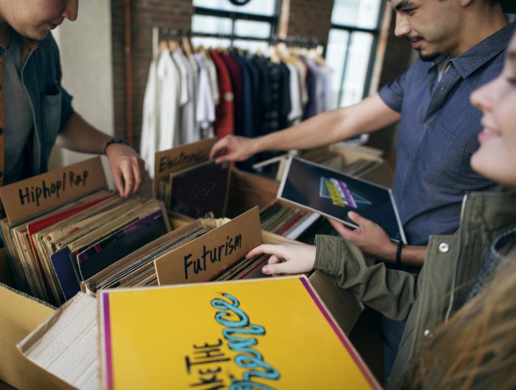 A group of friends in a record store are going through albums and talking about what they find. Concept: best cities for Millennials