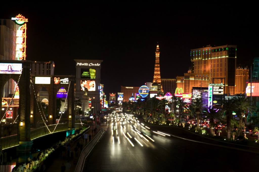 The Las Vegas Strip at night shows lit up casinos and blurry car headlights.