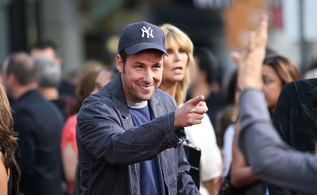 Adam Sandler pointing at some fans on the red carpet. Who Had The Better 4-Year Run During The 90s: Adam Sandler or Jim Carrey?