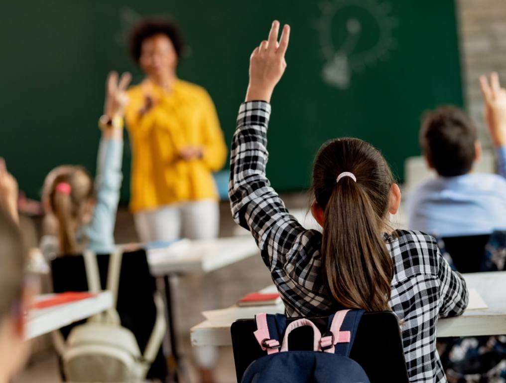 A young girl raising her hand in class at school.