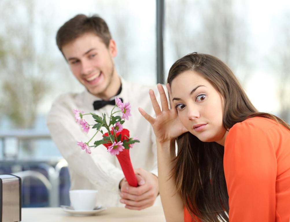 Disgusted woman rejecting a geek boy offering flowers in a blind date in a coffee shop interior