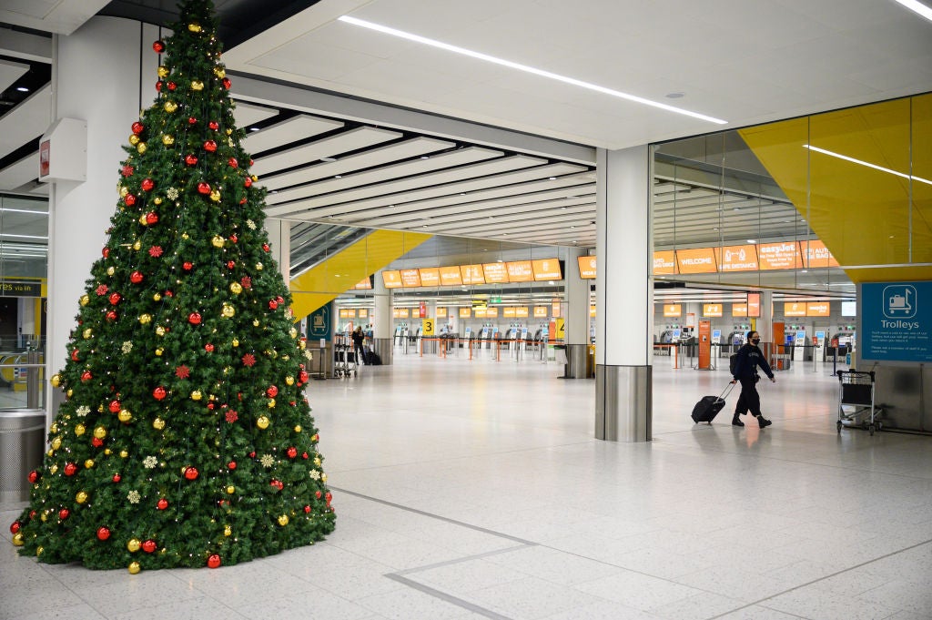 A person walks past the Christmas tree in the near-empty airport baggage claim area.