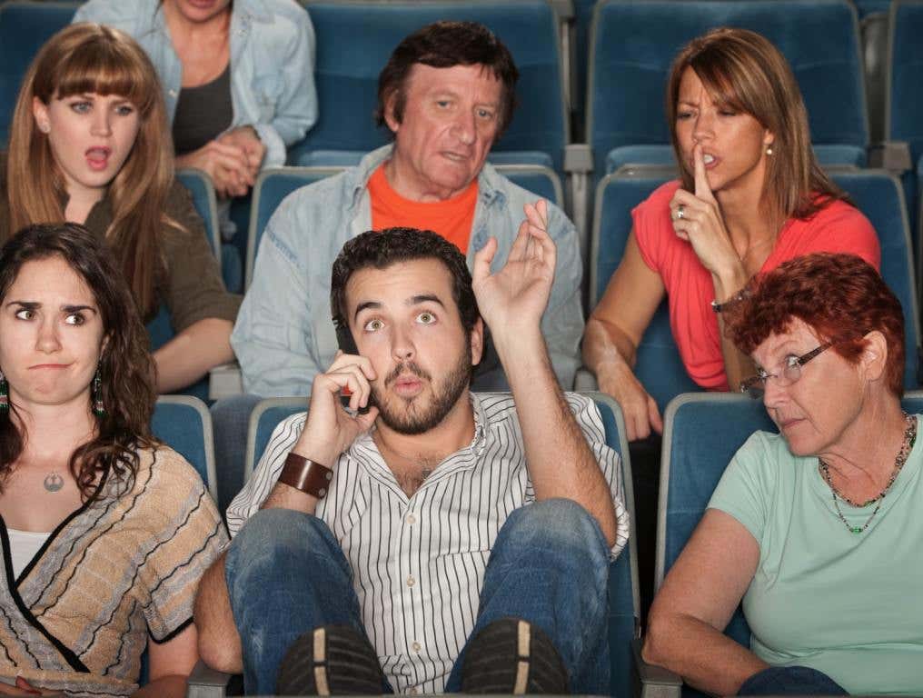 Guy talking on his phone at the movies.