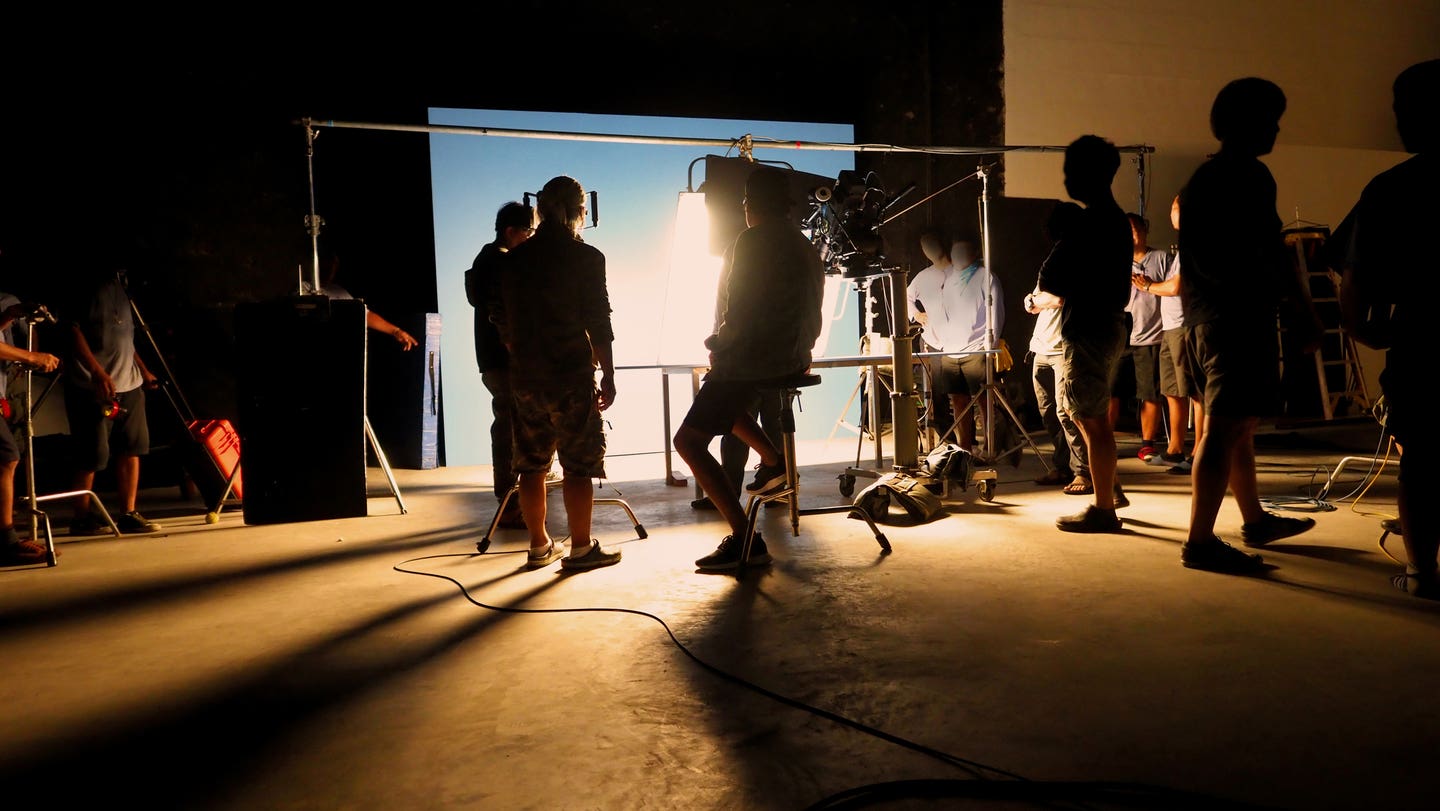 Silhouette images of video production behind the scenes of making of TV commercial movie shoot that film crew team lightman and camera man working together with director and equipment in big studio.