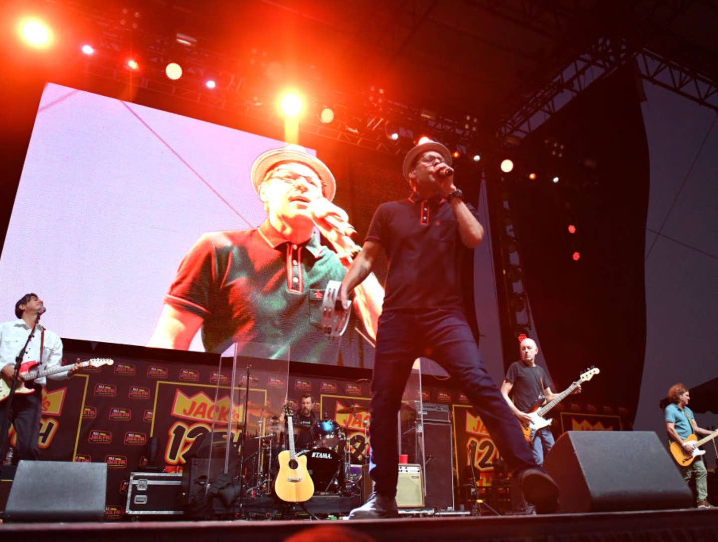 The Gin Blossoms perform on stage with lead singer Robin Wilson in front and guitar and drum players behind him.