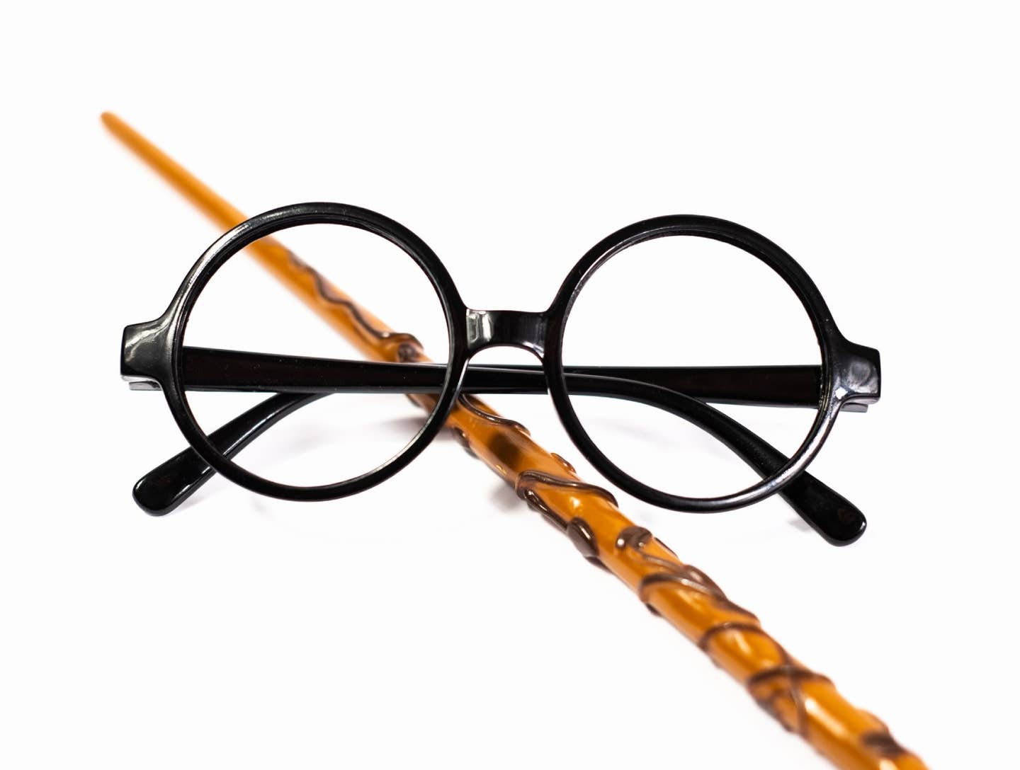 Round black eyeglasses and brown magic wand isolated on white background.