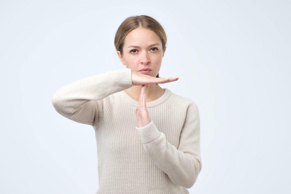 Young blonde woman in an ecru sweater is holding her hands up in a T formation, as if to say "time out".