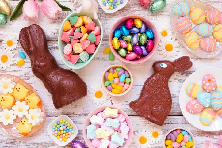 Chocolate bunnies, jelly beans and other traditional Easter candy sits in various white dishes that is spread out on a white wooden table. Though popular, these don't make the best Easter basket stuffers if you're trying to keep your kid healthy.