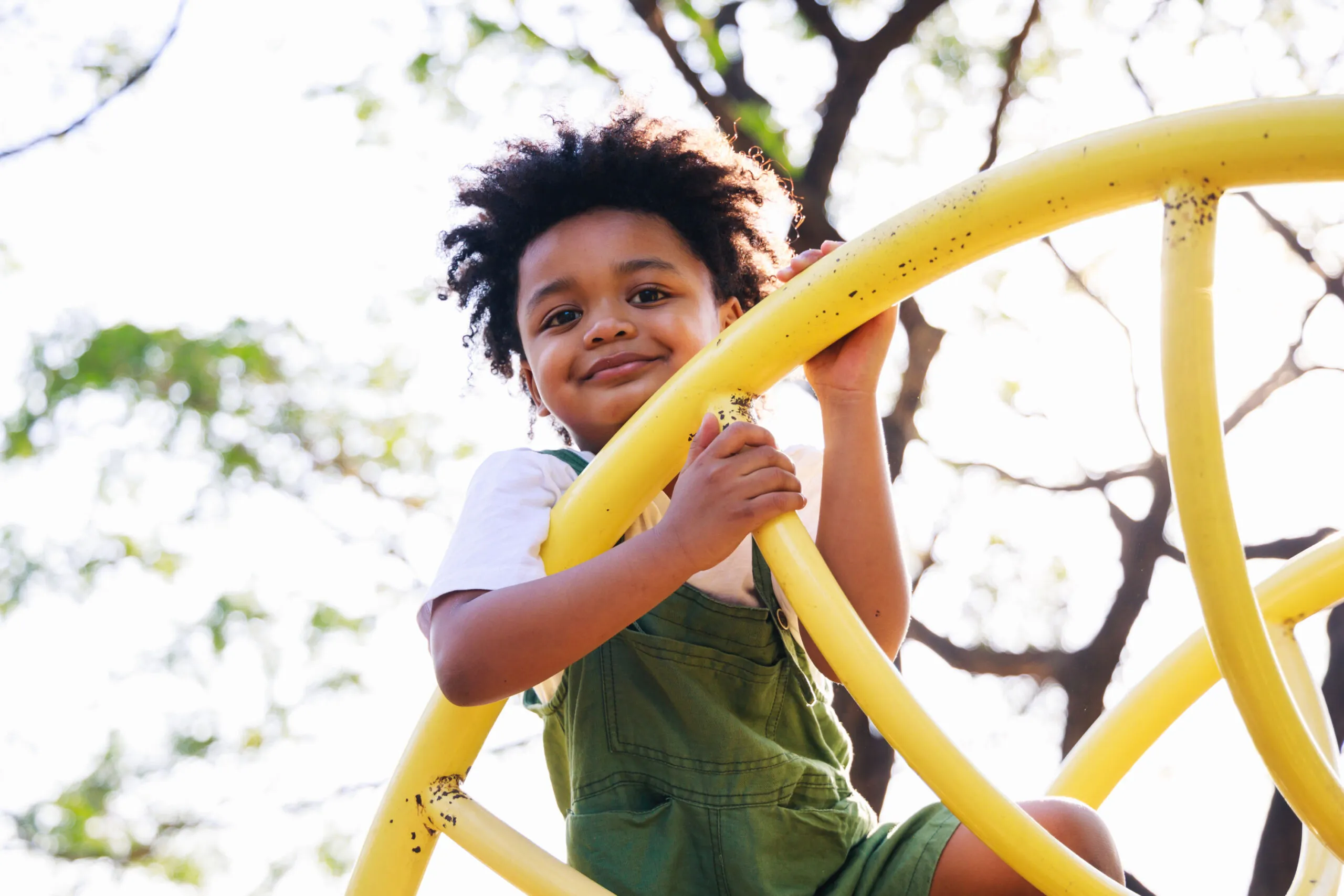 A young boy with brown hair climbing on a yellow jungle gym.