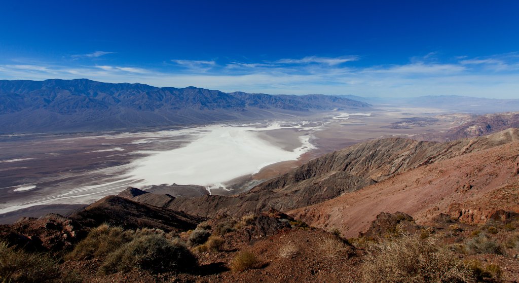 A mountain range in the foreground on the right, in front of a flat canyon below. The skies in the background are clear and blue.