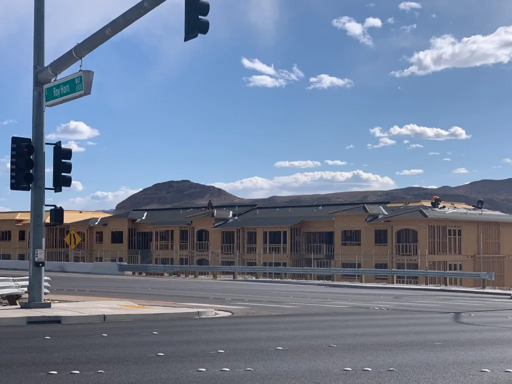 An apartment complex under construction is just wood and roof underlayment. The sky above is blue and there's a street sign at the corner intersection.