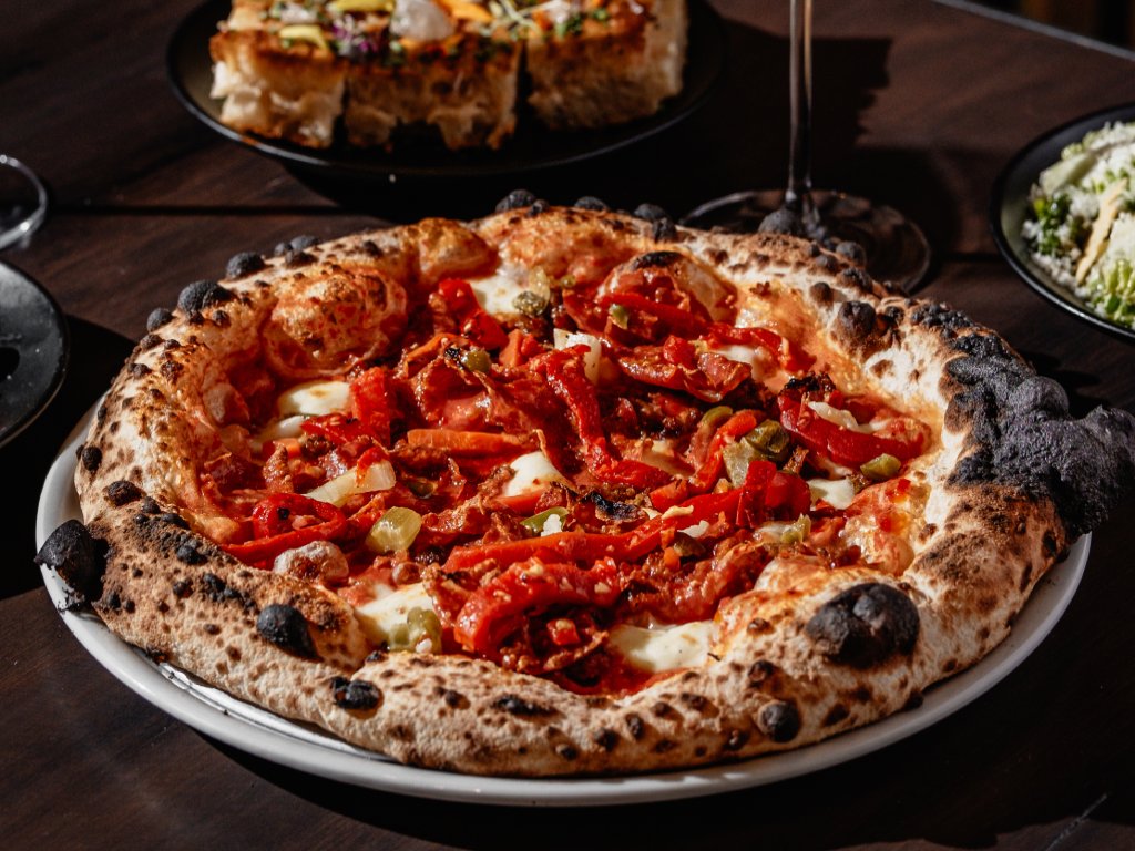 A well-cooked pizza sits on a pan topped with roasted red peppers. 