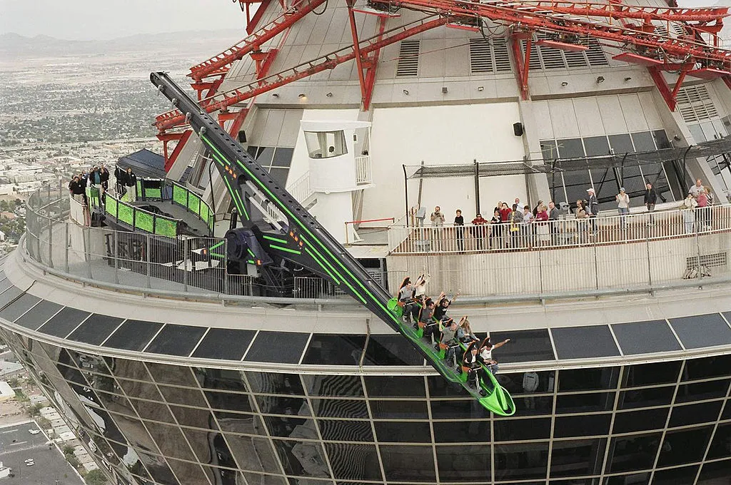 Close-up of a thrill ride on top of the STRAT hotel in Las Vegas. It looks like a green roller coaster hanging off the side of the tower.